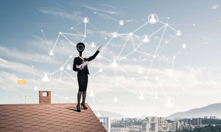 Faceless businesswoman with camera zoom instead of head standing on house roofの写真素材