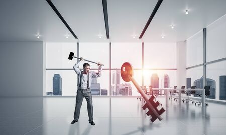Determined businessman in modern interior breaking with hammer stone key figureの写真素材