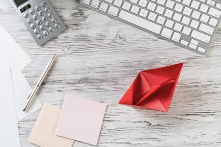 Businessman workspace at office desk with red paper ship. Top view office workplace background. Flat lay table with computer keyboard, calculator, business reports and pen. Main project managementの写真素材