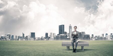 Funny man in red glasses and suit sitting on bench and reading bookの写真素材