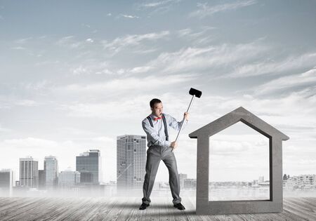 Determined businessman going to break with hammer house concrete figureの写真素材