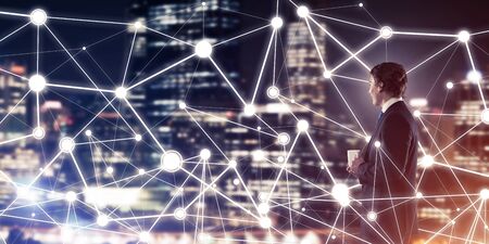 Businessman against night cityscape looking at social connection media conceptの写真素材