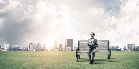 Funny man in red glasses and suit sitting on bench and reading bookの写真素材