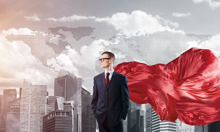 Young confident businessman wearing red cape against modern city backgroundの写真素材
