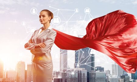 Young confident businesswoman wearing red cape against modern city backgroundの写真素材