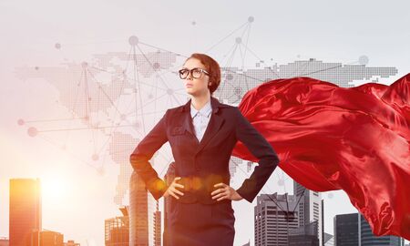 Young confident businesswoman wearing red cape against modern city backgroundの写真素材