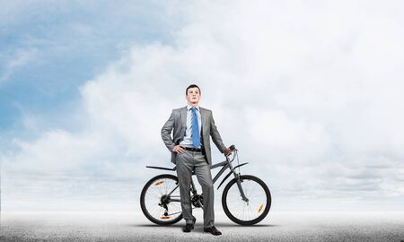 Office manager man wearing business suit standing with bike. Businessman with bicycle on background of cloudy blue sky. Male cyclist posing on camera with bicycle. Man relaxing outdoors in sunny day.の写真素材