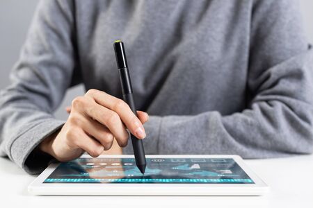 Woman using tablet computer for financial data analysis. Close-up of female hand holding pen and touching screen of tablet device. Online stock trading application. Mobile smart device in businessの写真素材