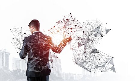 Businessman with documents pointing on abstract network with polygonal shapes. Back view of standing entrepreneur in business suit and tie. Professional business assistance and consulting service.の写真素材