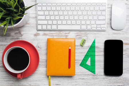 Top view designer table with office accessories. Morning coffee time and planning new day. Flat lay wooden desk with computer keyboard and mouse, smartphone, ruler, diary and green plant in pot.の写真素材