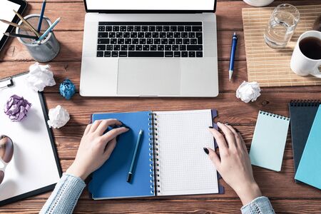 Female student taking notes with pen at desk. Business research and education. Flat lay office workplace with accessories, businesswoman hands and laptop. Online conference or webinar mockup.の写真素材