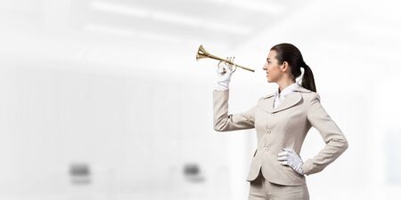 Business woman playing trumpet brass. Young lady in white business suit and gloves posing with music...