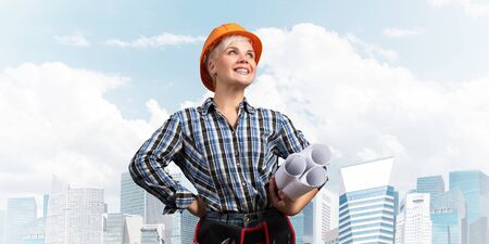 Attractive female engineer in hardhat standing with technical blueprints. Portrait of happy young...