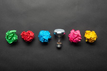 Lightbulb and crumpled colorful paper balls on black background. Successful solution of problem....