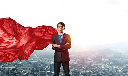 Young confident businessman wearing red cape against modern city backgroundの写真素材