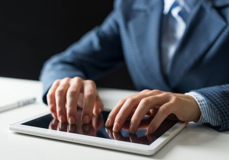 Close-up of male hands typing on digital tablet touch screen. Man in business suit sitting at desk and working at tablet computer. Manager at workplace in office. Business and digital technologyの写真素材