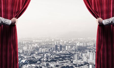 Hands of businessman opening red velvet curtain and cityscape at backgroundの写真素材