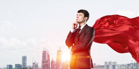 Young pensive businessman wearing red cape against modern city backgroundの写真素材