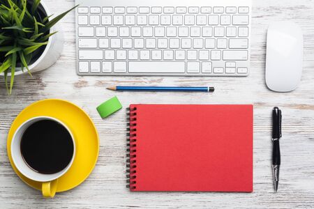 Top view conference table with office accessories. Break time at workplace. Flat lay wooden desk with computer keyboard and mouse, cup of coffee, spiral notebook and green plant in pot.の写真素材