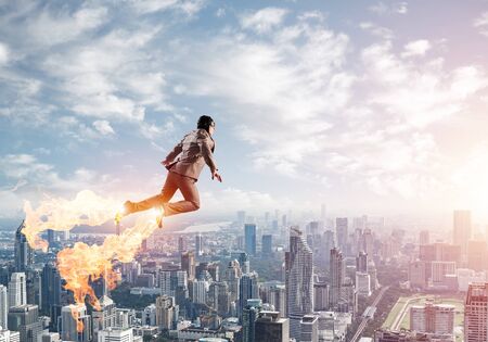 Businessman in suit and aviator hat flying in blue sky as superheroの写真素材