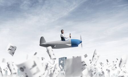 Successful management and information analysing concept with funny pilot. Aviator driving propeller plane above falling paper sheets with diagrams. Young man flying in small airplane above paperwork.の写真素材