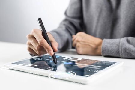 Woman using tablet computer for project management. Close-up of female hand holding pen and touching screen of tablet device. Online stock trading and investing. Mobile smart device in businessの写真素材