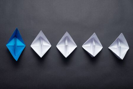 Row of paper ships on black background. Leadership concept with blue paper ship leading among white. Individual motivation and direction. Social marketing layout with copy space.の写真素材