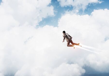 Businessman in suit and aviator hat flying in blue sky as superhero. Corporate manager as launching upwards with jet flame in stratosphere. Successful business startup motivation conceptの写真素材