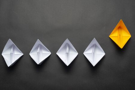 Row of paper ships on black background. Business concept of creative innovation and leadership. Flat lay yellow origami leader boat ahead others boats. Social marketing layout with copy space.の写真素材