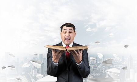 Surprised businessman holding book with open mouth.
