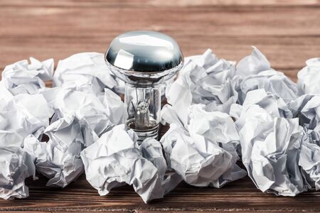 Incandescent bulb and crumpled white paper balls on brown wooden tableの写真素材