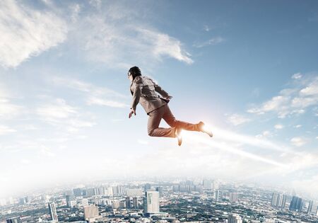 Businessman in aviator hat flying in blue sky as superheroの写真素材