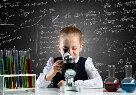 Little girl scientist looking through microscope in classroom at chemistry lesson. School chemical...