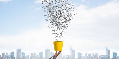Various letters flying out from yellow pot. Human hand holding pot with brain on modern cityscape background. Information flow and creative idea generation. Business education and knowledge.の写真素材