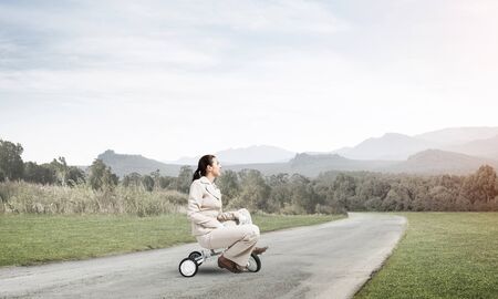 Beautiful caucasian woman riding kids bicycle on asphalt road. Young employee in white business suit...