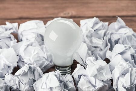 Incandescent bulb and crumpled white paper balls on brown wooden tableの写真素材