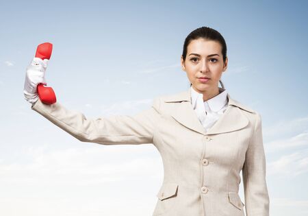 Businesswoman holds vintage red phone on distance. Serious operator in business suit posing with telephone on blue sky background. Employee ignores communication. Business assistance and support.の写真素材