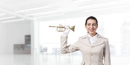 Beautiful woman holding trumpet brass near ear and listening. Young businesslady in white business...