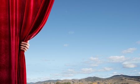 Human hand opens red curtain on natural landscape backgroundの写真素材