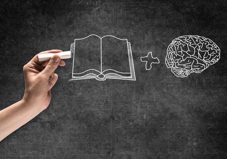 Businessman hand with chalk draws education process sketch on chalkboard. Freehand white chalk illustration on blackboard. Human brain and open book symbols. Brainstorming business ideas conceptの写真素材