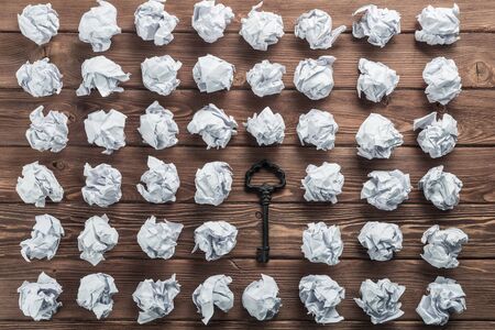 Vintage key among many balls of crumpled paper on wooden tableの写真素材