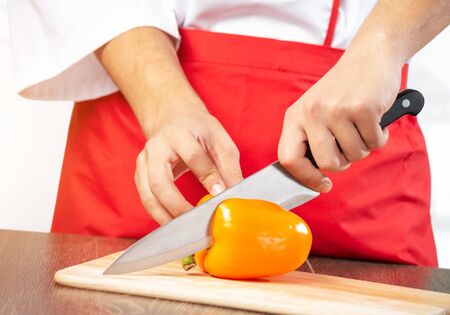 Chef hands cutting orange fresh pepper on wooden board. Close up man hands cooking with knife on table in kitchen. Vegetarian food and organic healthy ingredients. Restaurant food preparation.の写真素材