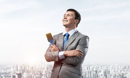 Confident and creative businessman painter standing with arms folded. Portrait of happy handsome man in business suit and tie on cityscape background. Ambitions and creativity in business.の写真素材