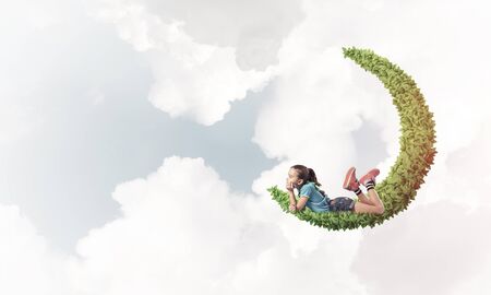 Cute kid girl on green moon floating in day skyの写真素材