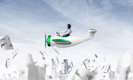 Successful management and information analysing concept with funny pilot. Aviator driving propeller plane above falling paper sheets with diagrams. Young man flying in small airplane above paperwork.の写真素材