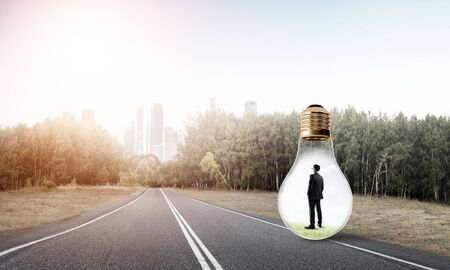 Young businessman trapped inside of light bulb on asphalt roadの写真素材