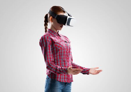 Young woman in checked shirt wearing virtual helmet against gray backgroundの写真素材