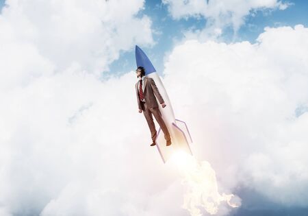 Business person in suit launching upwards on rocket. Progress and innovation technology. Corporate employee flying with jetpack rocket in stratosphere. Leadership motivation and goal achievement.の写真素材