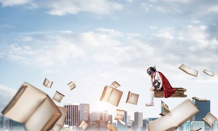 Little sad child in mask and cape floating on book in skyの写真素材