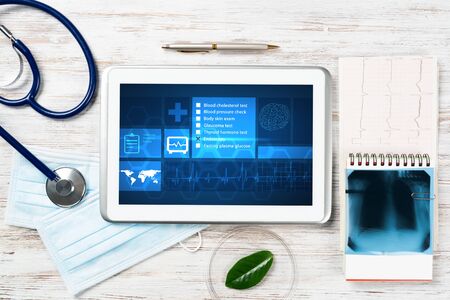 Modern social health insurance program. Tablet computer with healthcare application interface on screen. Stethoscope, x-ray image and cardiogram on wooden desk. Digital healthcare technologies.の写真素材